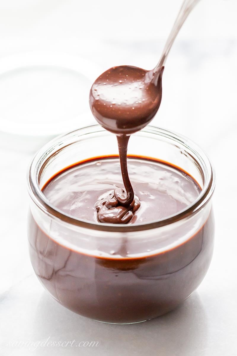 A jar of hot fudge sauce being drizzled from a small ladle