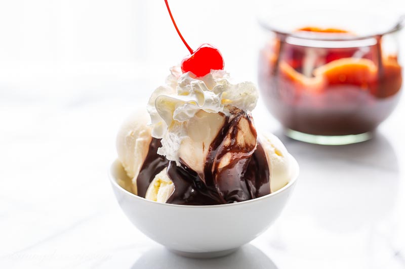 A small bowl with scoops of vanilla ice cream, hot fudge sauce, whipped cream and a cherry