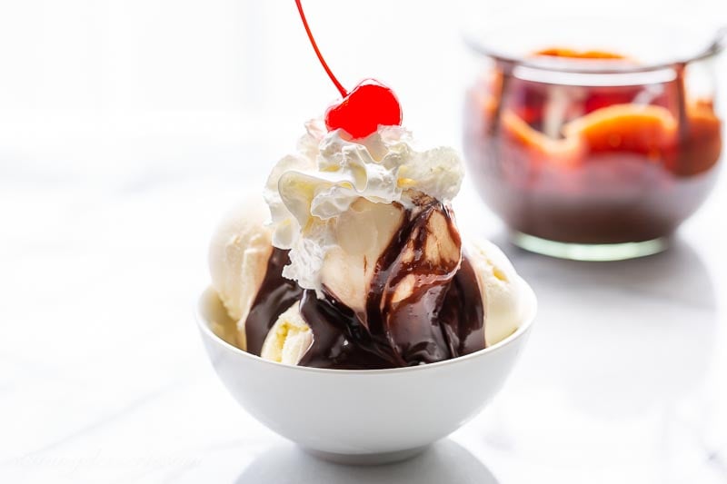 A small bowl with scoops of vanilla ice cream, hot fudge sauce, whipped cream and a cherry
