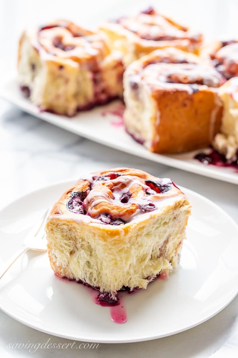 A plate with a flaky lemon blueberry sweet roll and a fork