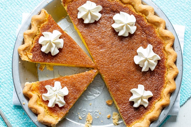 A sliced lemon chess pie topped with swirls of whipped cream