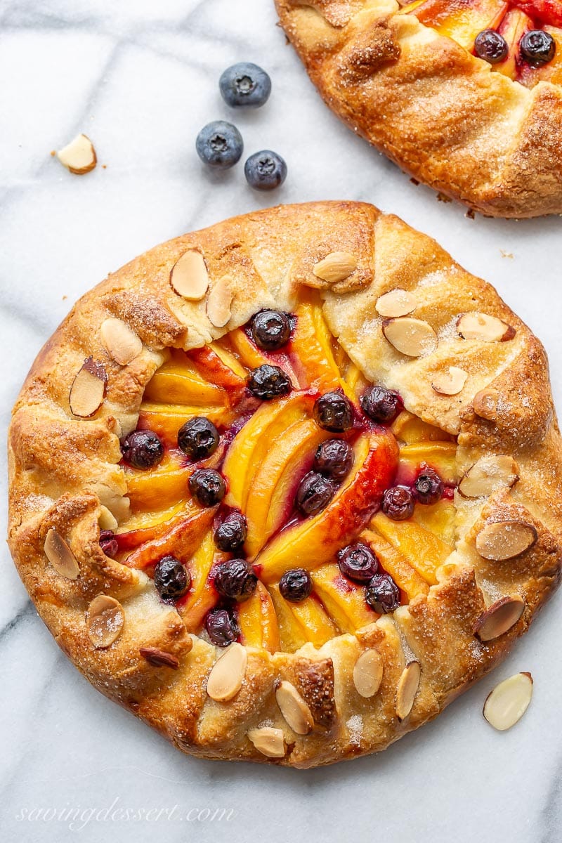 An overhead view of a rustic peach tart with blueberries and sliced almonds