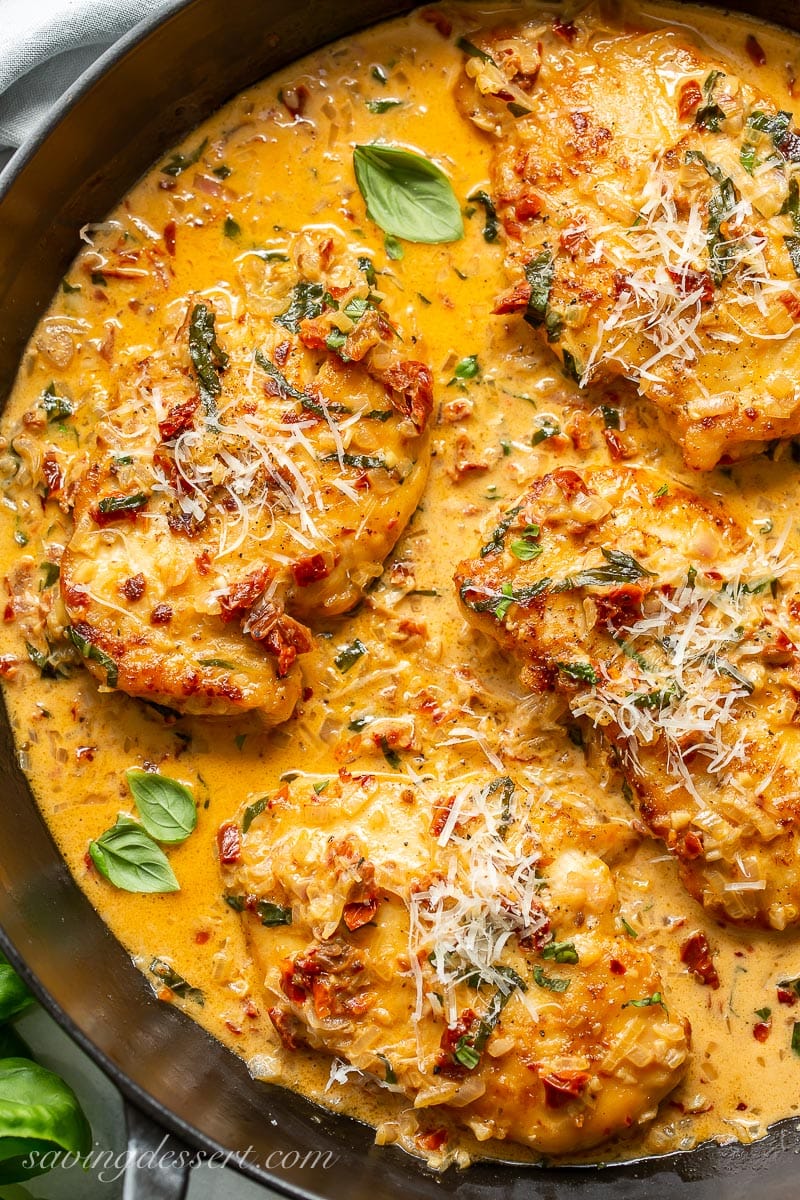 A close up of chicken in a skillet with a sun-dried tomato cream sauce