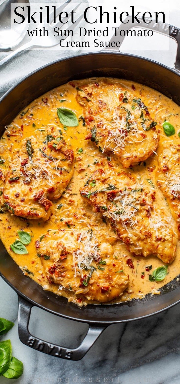 A close-up of a skillet with chicken breasts in a sun-dried tomato cream sauce with fresh basil