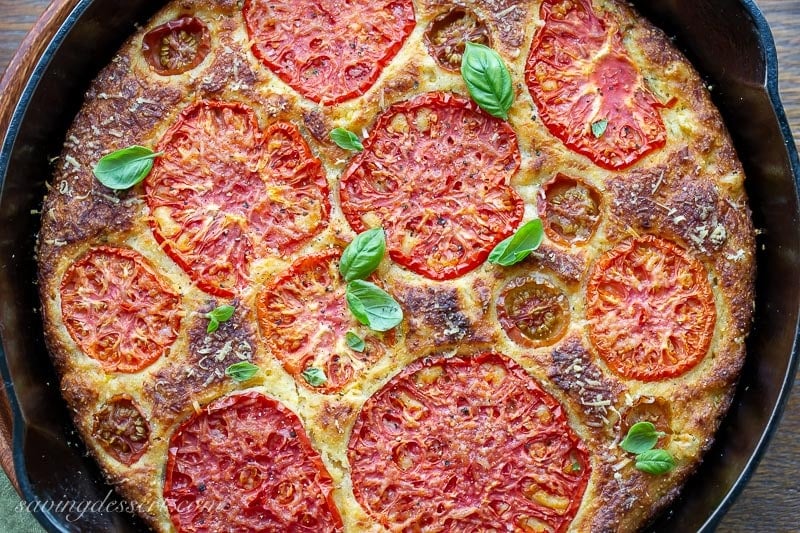 A skillet with cornbread topped with tomatoes, cheese and basil