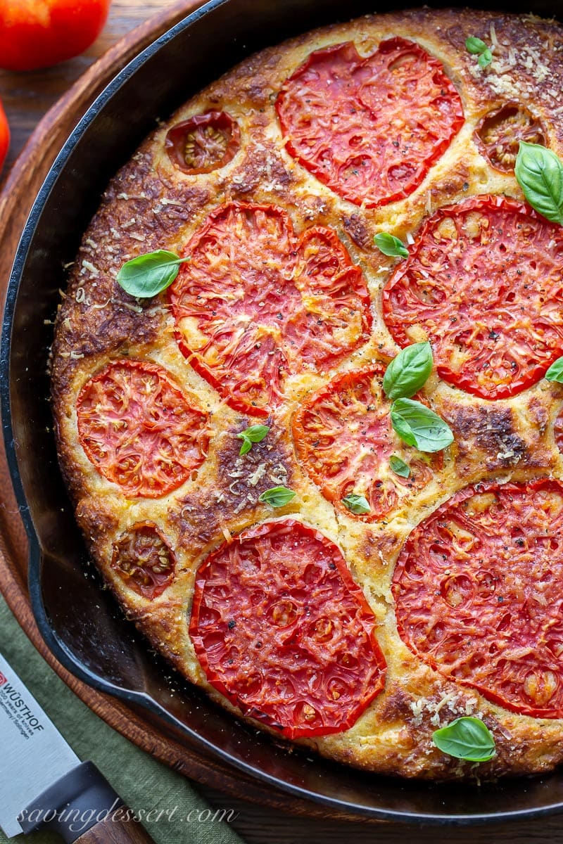 An overhead view of a skillet of cornbread topped with tomatoes and basil leaves