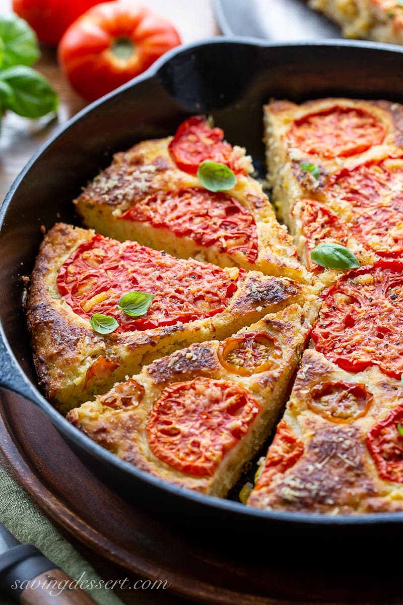 A side view of a cast iron skillet filled with sliced cornbread topped with tomatoes and fresh basil leaves