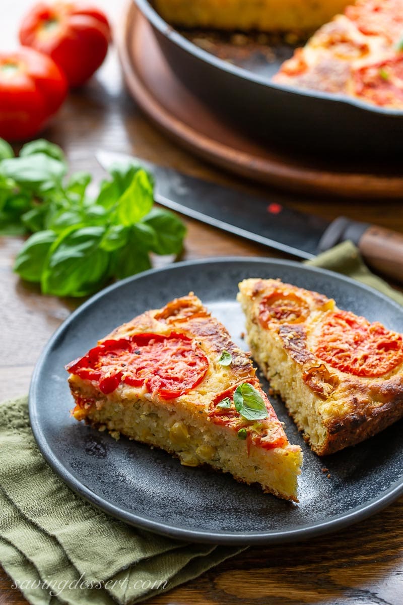 Two slices of tomato topped cornbread with fresh basil