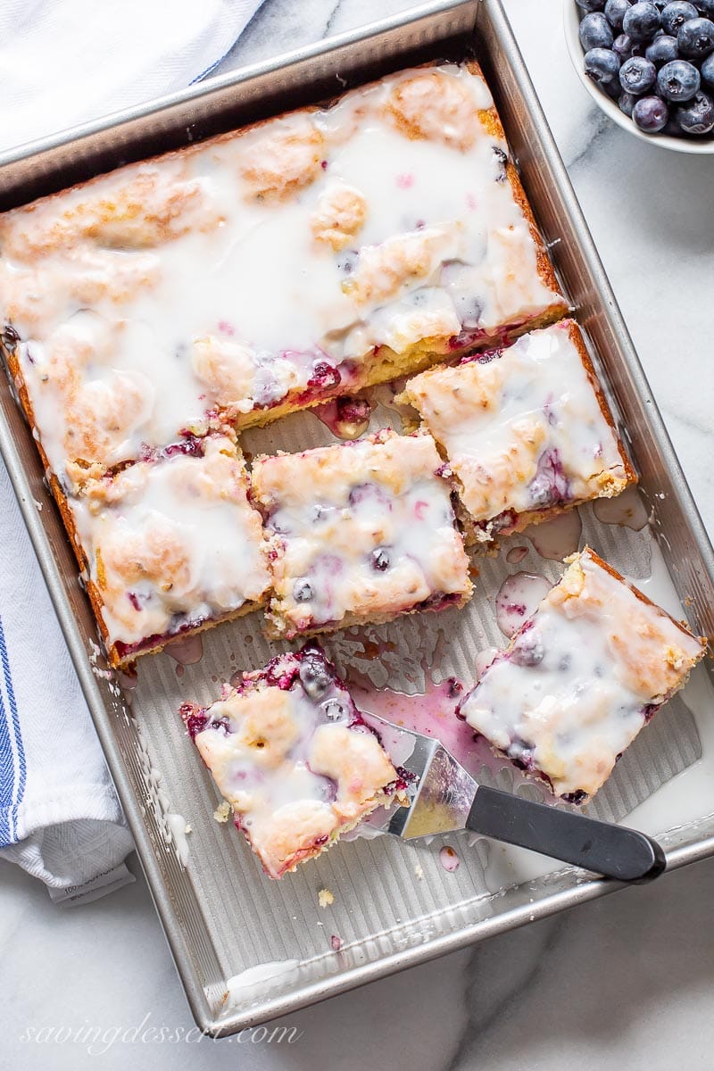 A pan with sliced blueberry cake and a spatula with a buttermilk glaze on top