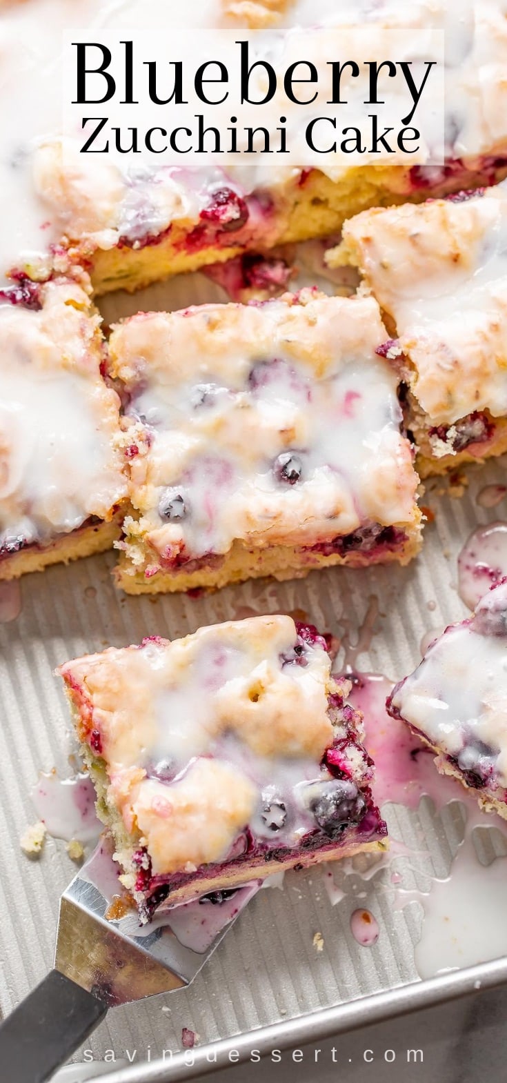 A sliced zucchini cake in a pan with blueberries on top and a simple buttermilk glaze