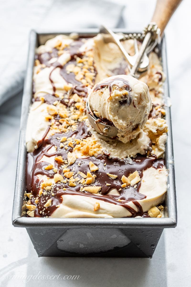 A pan of ice cream with a scoop topped with chocolate sauce and peanuts
