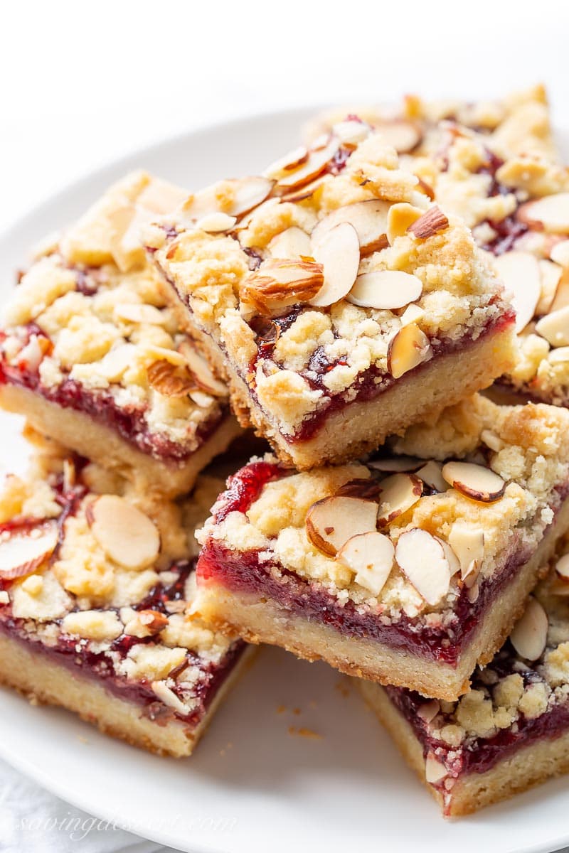 A plate stacked with raspberry bars topped with sliced almonds