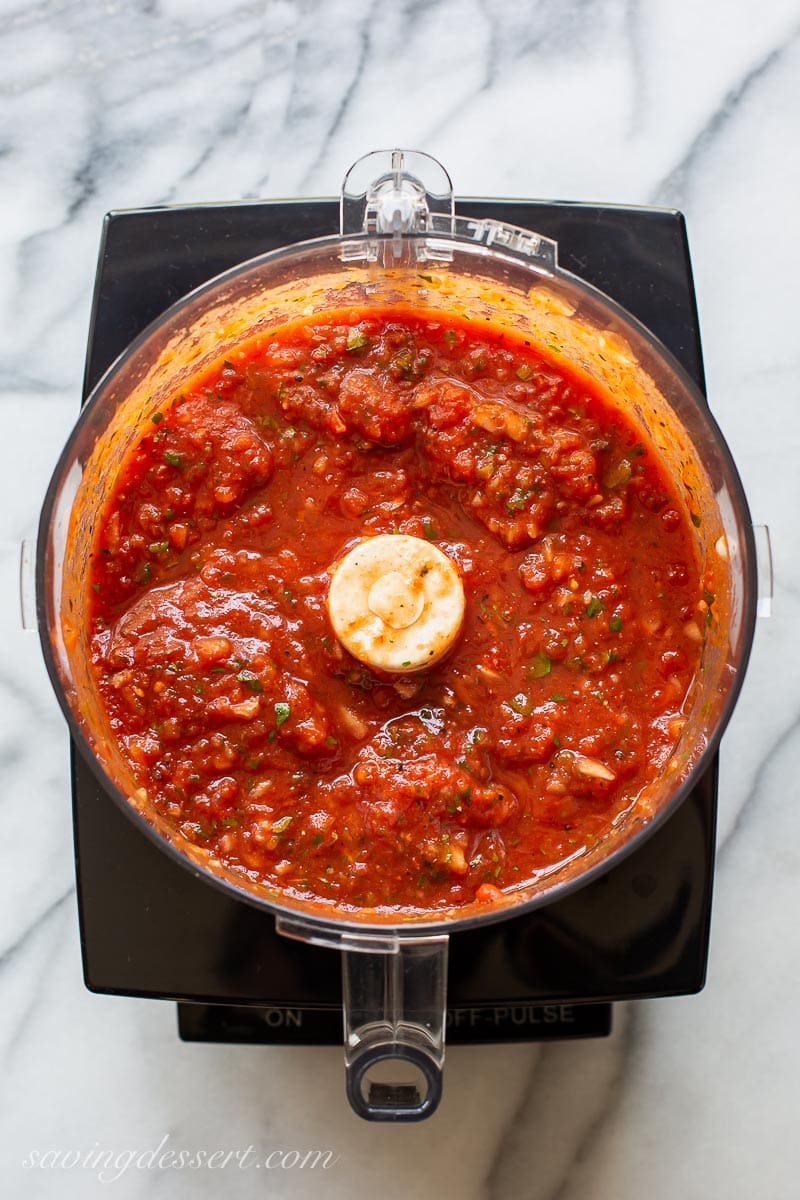 The bowl of a food processor filled with freshly made tomato salsa