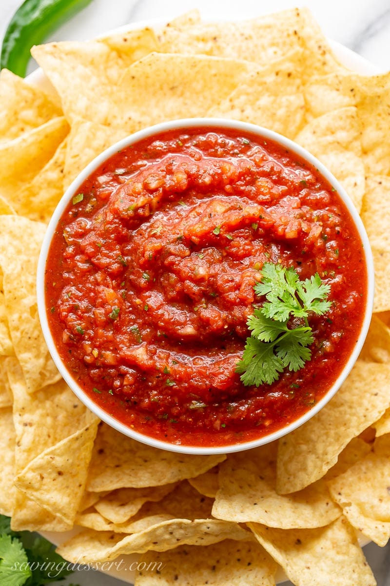 An overhead view of a bowl of restaurant style salsa garnished with cilantro and served with chips