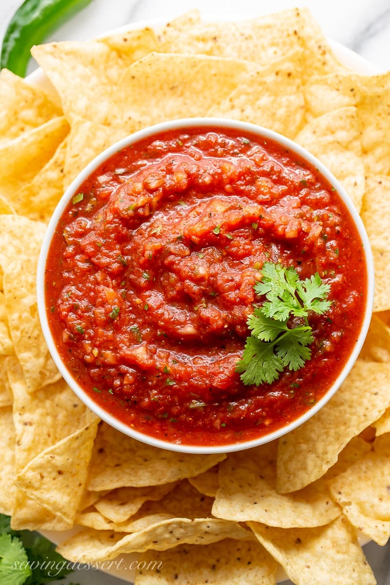 An overhead view of a bowl of restaurant style salsa garnished with cilantro and served with chips