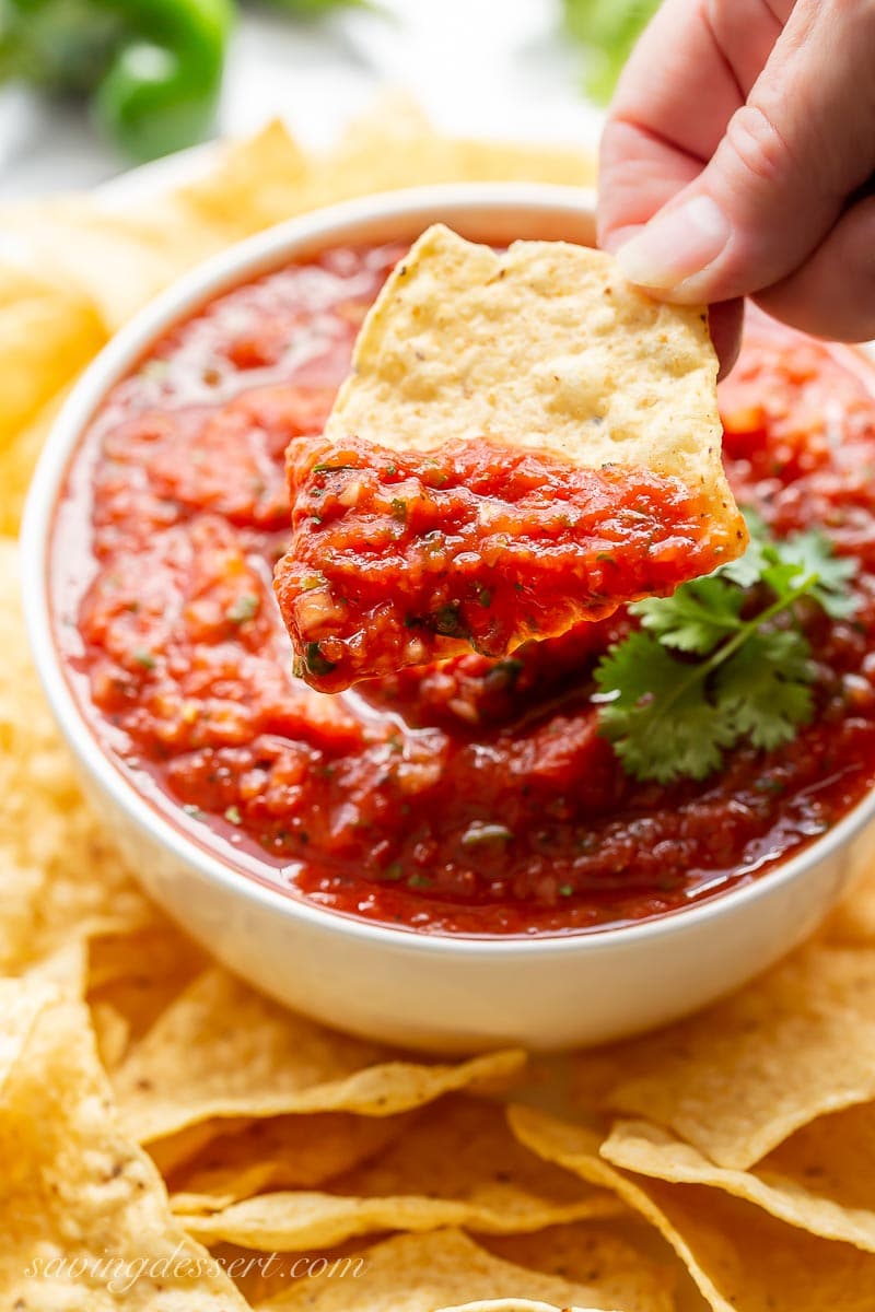 A bowl of salsa with a tortilla chip scooping out a bite