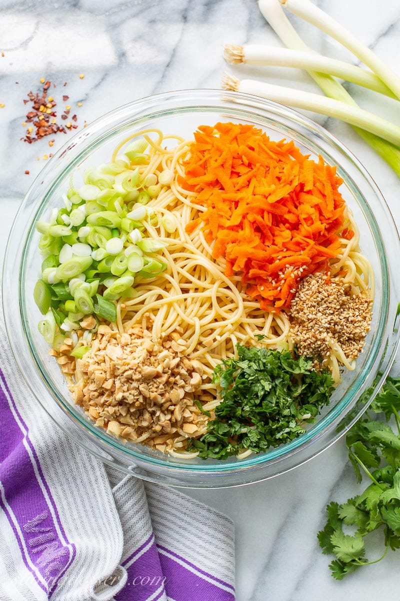 An overhead view of a bowl with carrots, onions, peanuts and cilantro over spaghetti