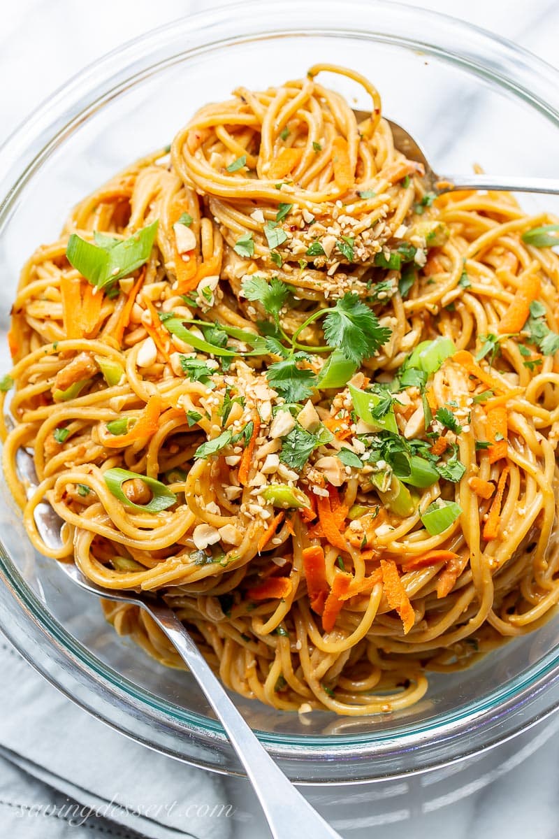 A bowl of spaghetti covered in a spicy peanut sauce and garnished with cilantro, carrots and sesame seeds