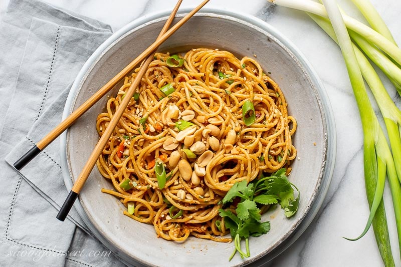 A bowl of spicy peanut noodles garnished with peanuts and cilantro with chopsticks