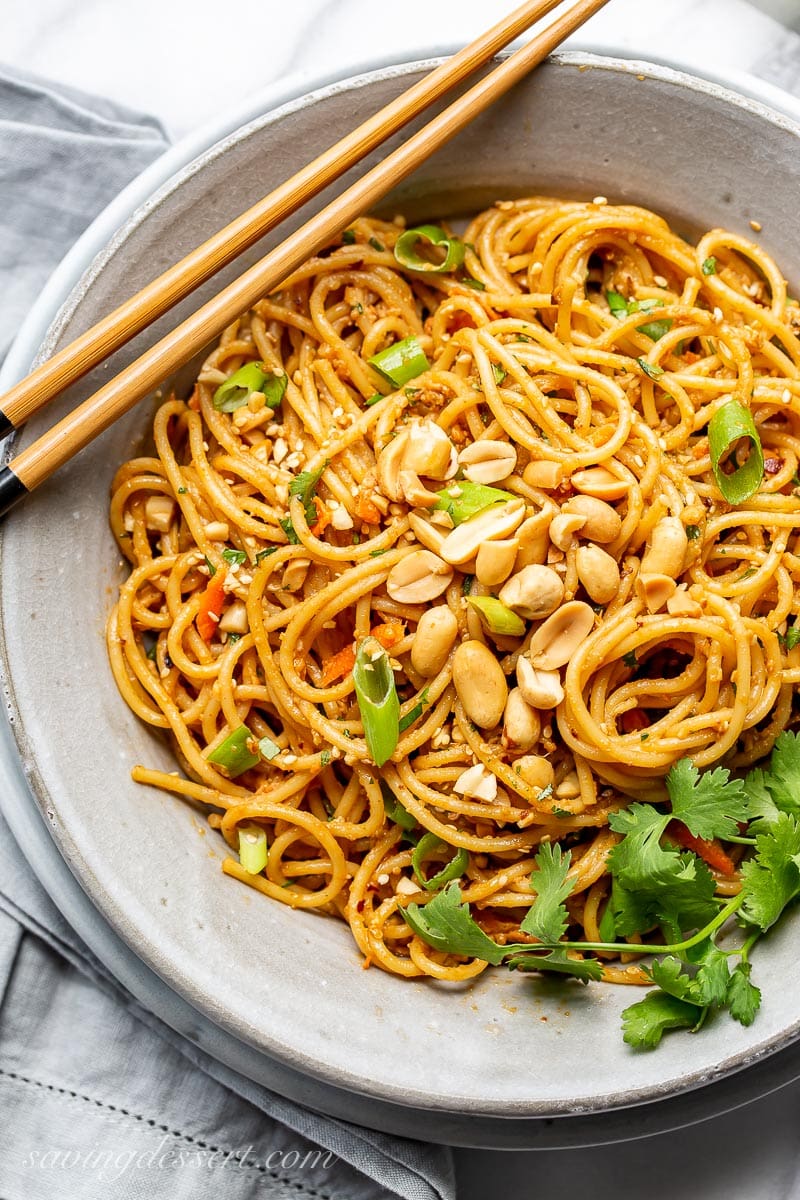 An overhead view of a bowl of spicy peanut noodles garnished with peanuts and cilantro