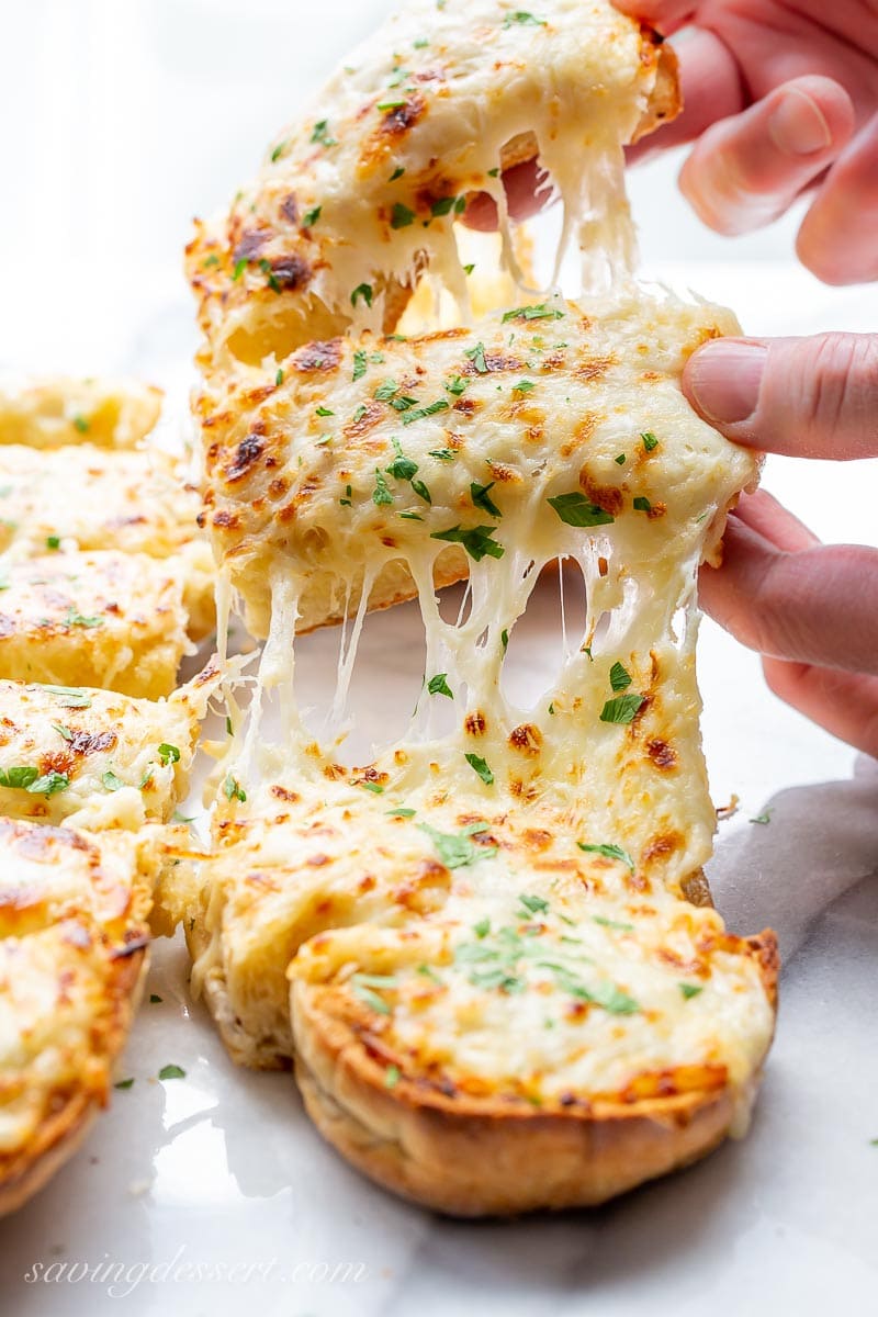 Slices of cheesy garlic bread being lifted from a toasted loaf