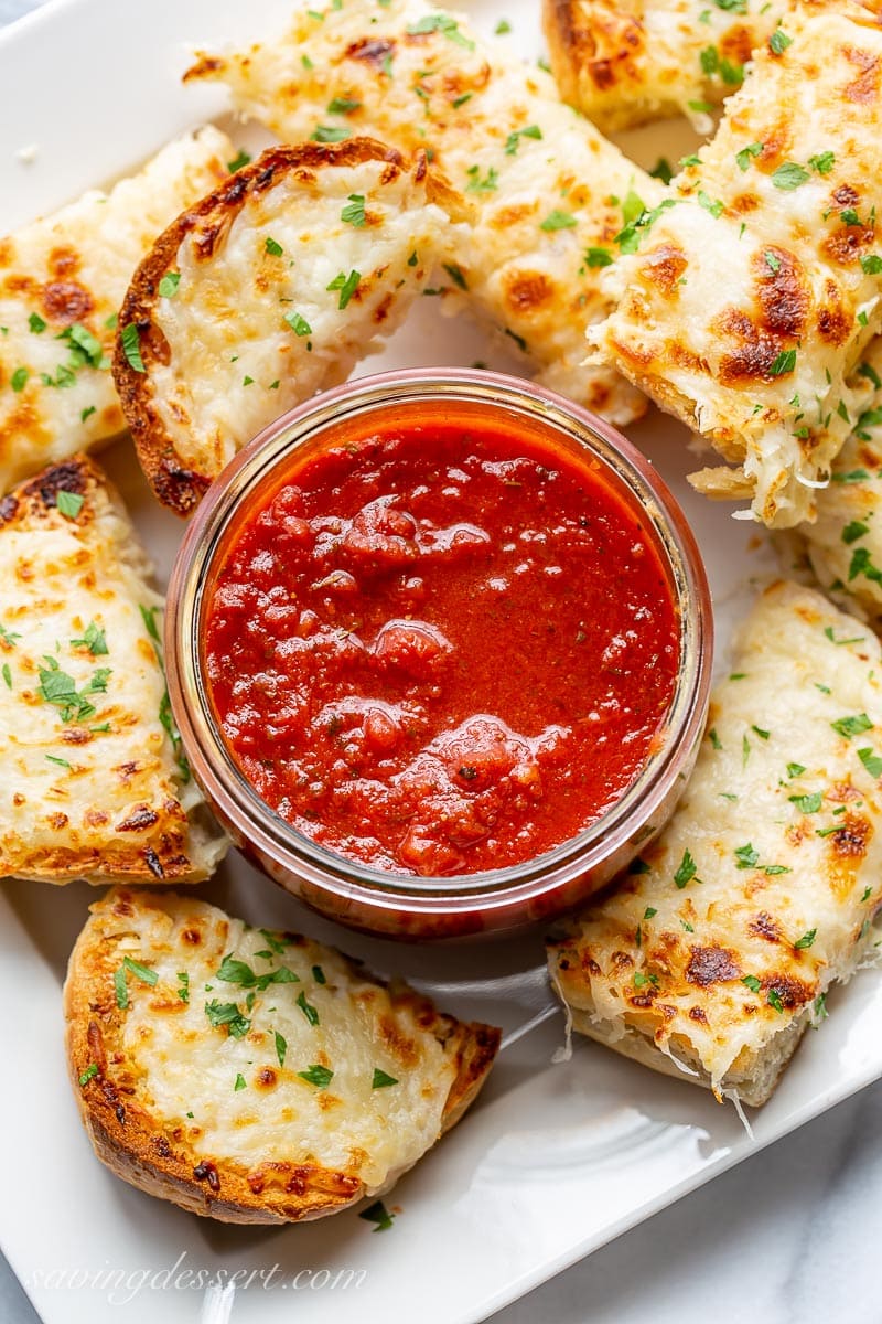 An overhead view of a platter of garlic bread topped with cheese and served with marinara sauce