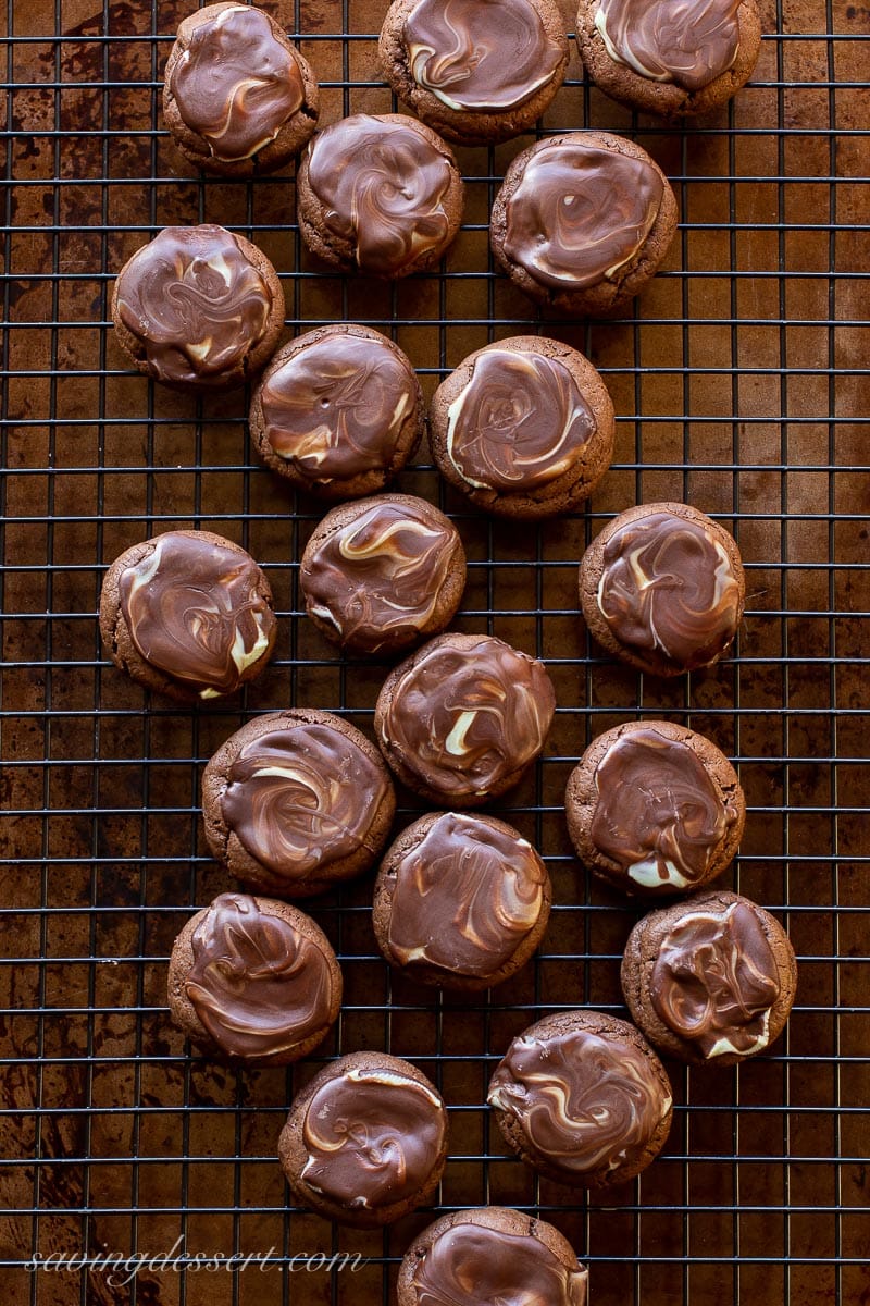 A cooling rack covered with chocolate cookies with melted chocolate mints swirled on top