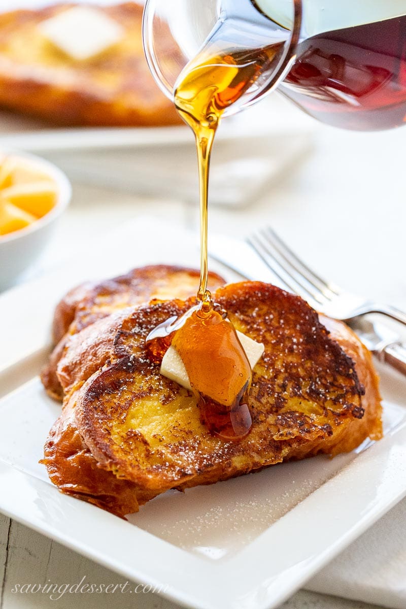 A plate of French toast topped with a pat of butter being drizzled with syrup