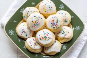 A holiday plate filled with Ricotta cookies topped with icing and sprinkles