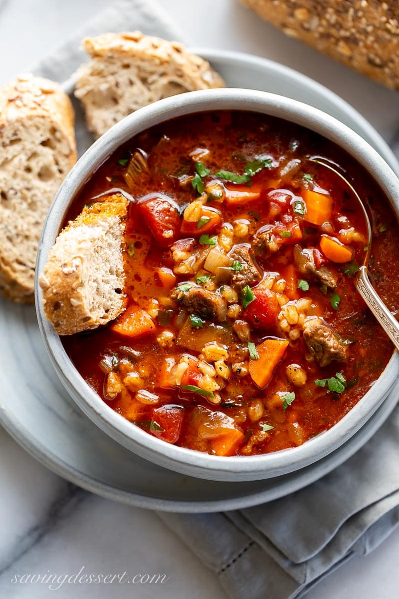 A bowl of beef barley soup with a slice of bread dipped in the broth