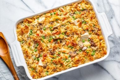 A casserole dish filled with chicken and noodles with peas and carrots
