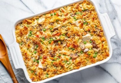 A casserole dish filled with chicken and noodles with peas and carrots