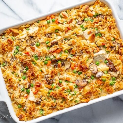 A casserole dish filled with chicken and noodles with peas and carrots