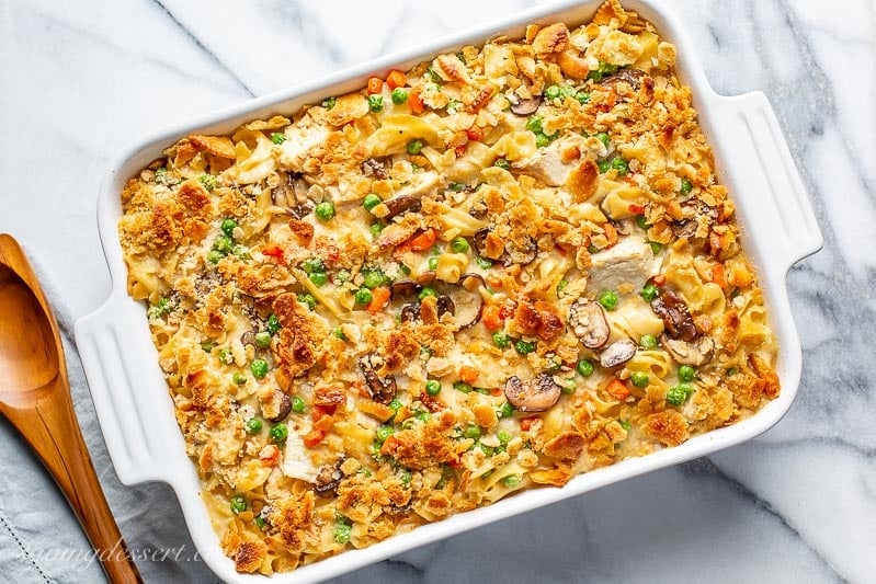 A casserole dish filled with chicken and noodles with peas and carrots