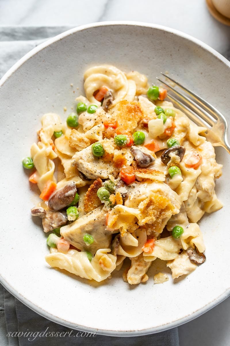 A bowl of chicken, egg noodles, peas, carrots and mushrooms in a cheesy white sauce