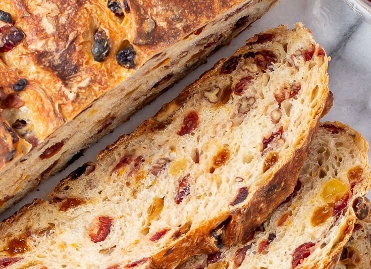 A round loaf of Harvest Bread sliced showing cranberries, nuts and raisins