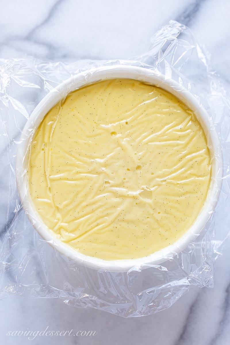 A bowl of vanilla pudding with plastic wrap pressed onto the surface