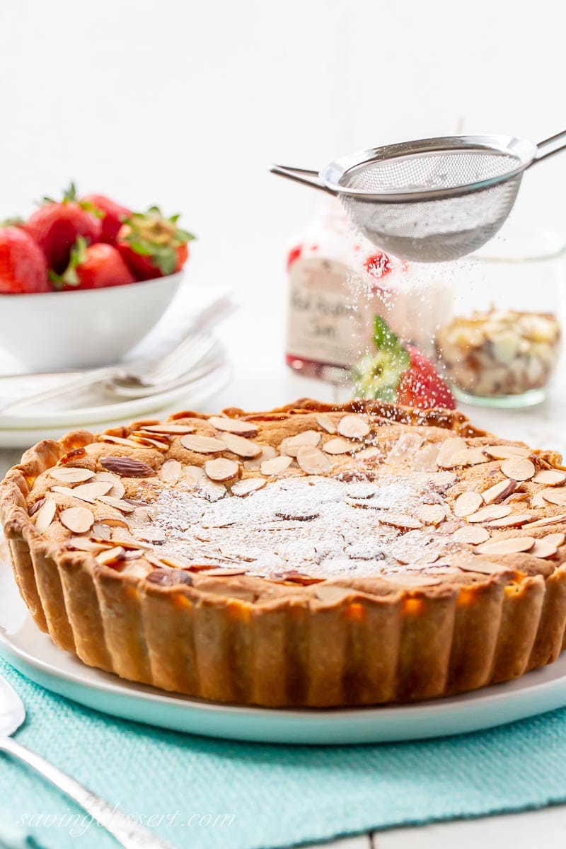 An almond topped tart being dusted with powdered sugar