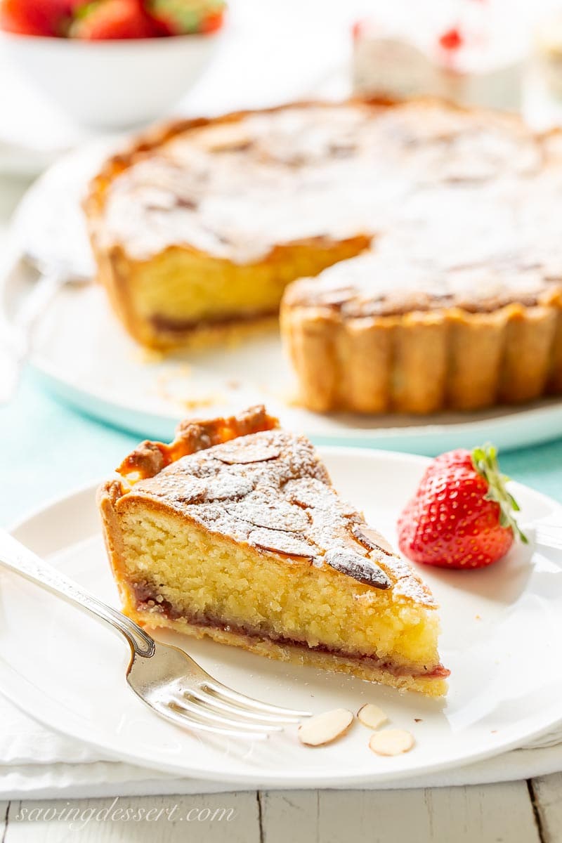 A slice of an almond topped Bakewell Tart on a plate with a strawberry