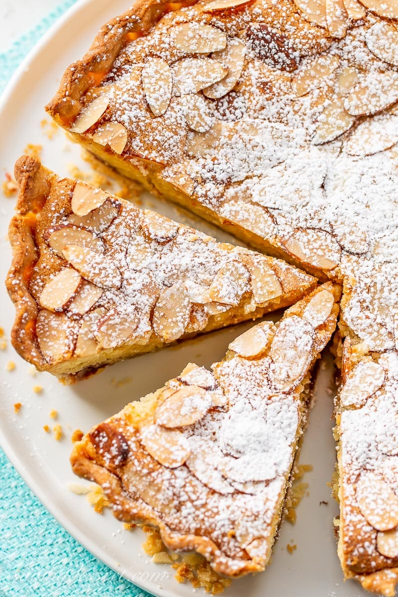 An overhead view of a sliced tart topped with almonds and dusted with powdered sugar