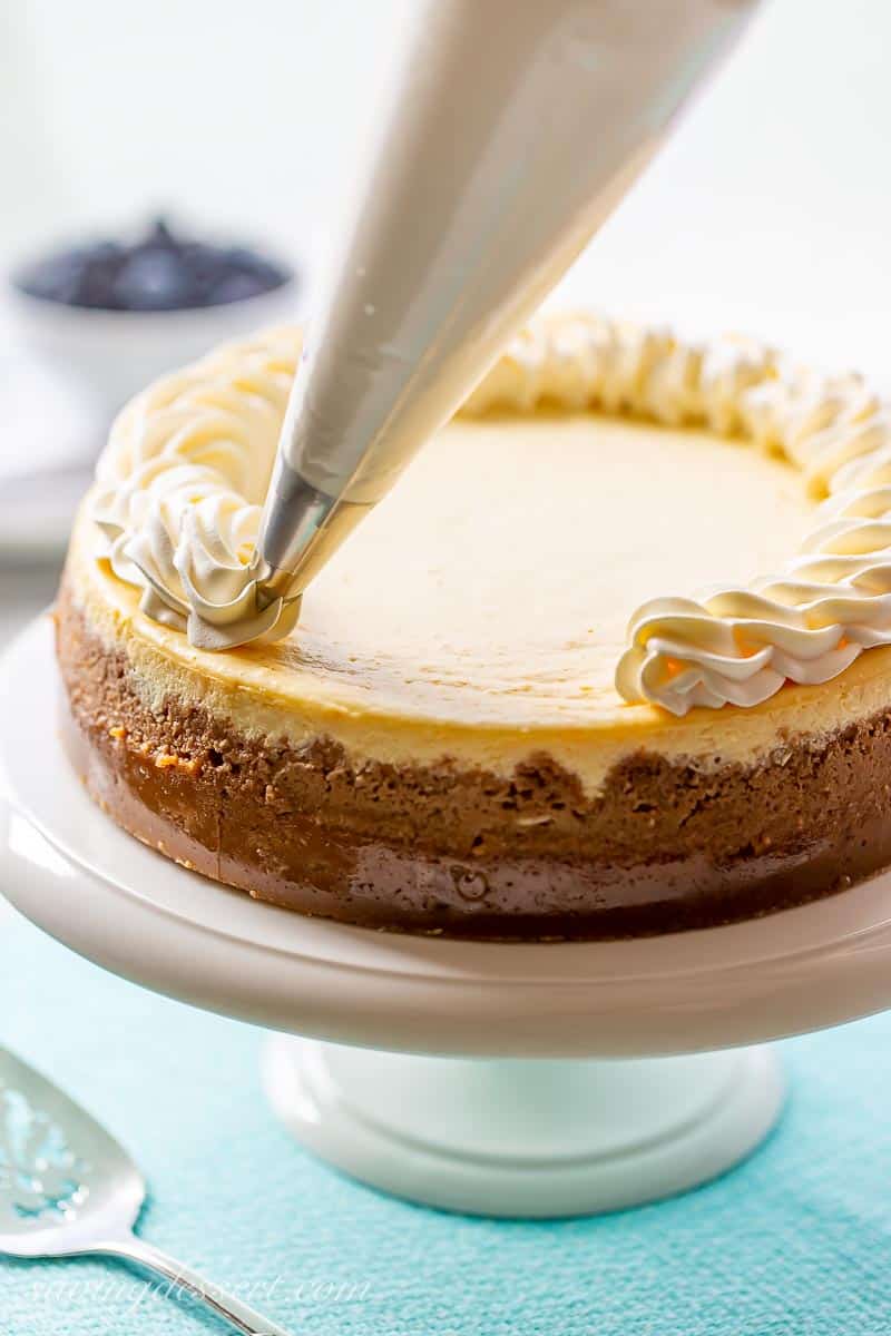 New York Style cheesecake being topped with swirls of whipped cream