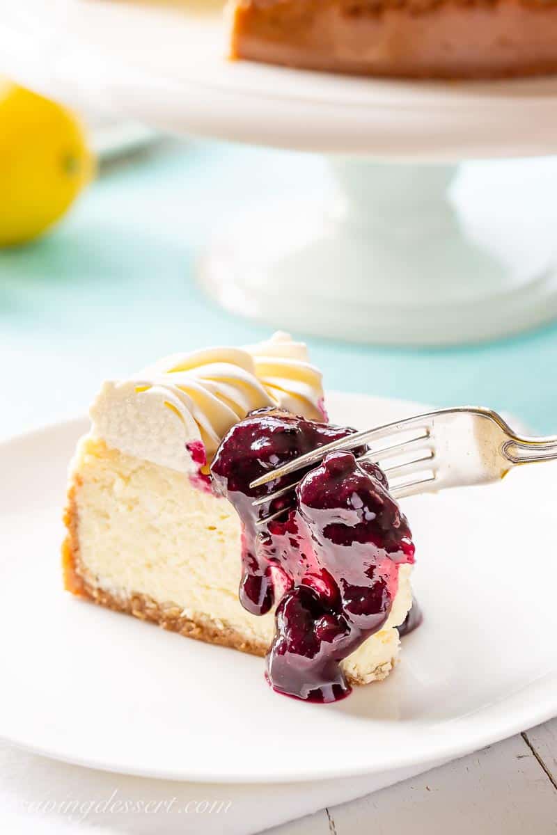 A slice of cake topped with blueberry sauce being cut with a fork