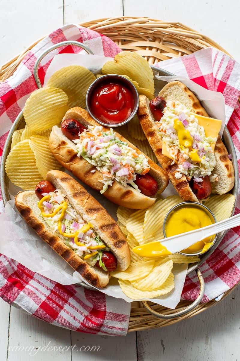 A platter of grilled hot dogs topped with coleslaw onions and mustard. Served with chips