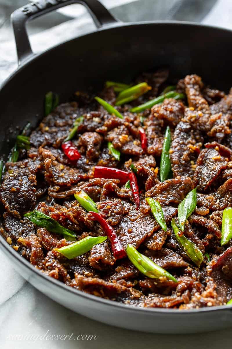 A skillet filled with sliced beef with green onions and peppers