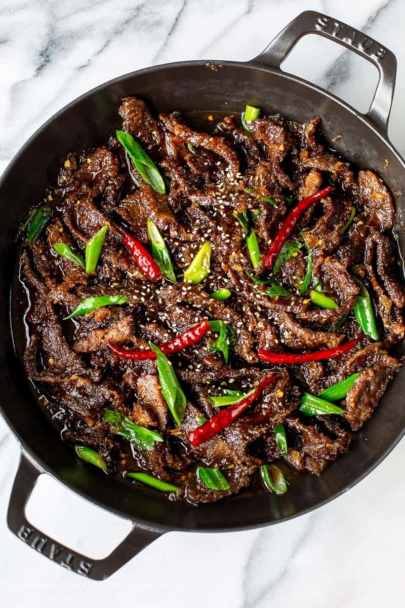 An overhead view of a skillet filled with red peppers, green onions and sliced Mongolian Beef