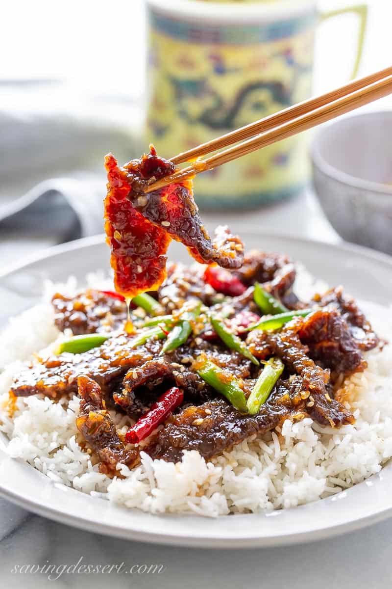 Chopsticks picking up a slice of Mongolian Beef covered in a sweet hot sticky sauce