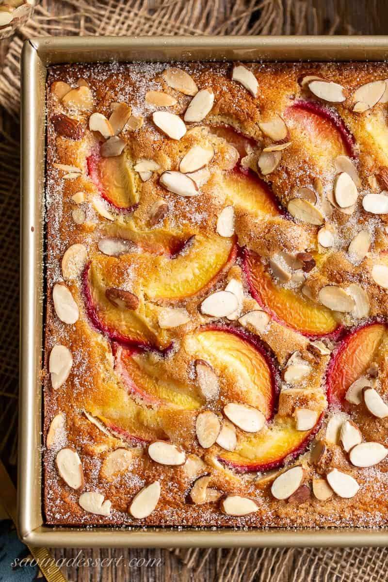 A square pan filled with peach cake topped with fresh sliced peaches and sprinkled with sliced almonds