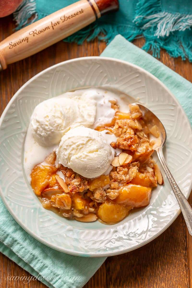 A bowl of warm Peach Crisp topped with scoops of ice cream and sliced almonds