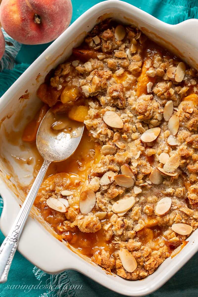 A square casserole dish filled with peaches and a crisp topping with oats and almonds