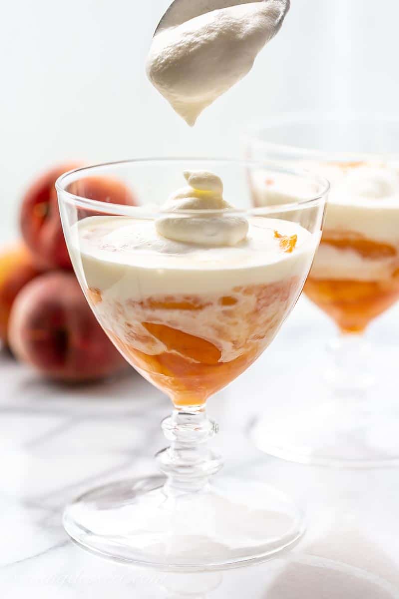 A glass of peaches with lightly whipped cream on top